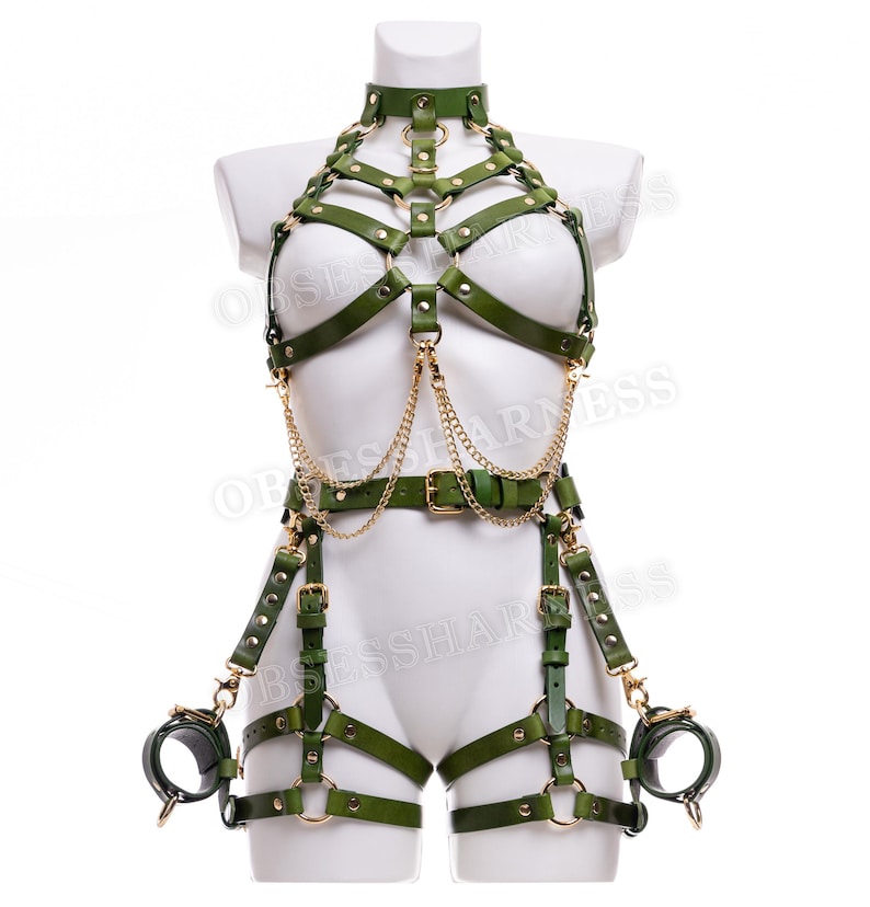 May include: A green leather harness with gold hardware and chains. The harness includes a chest piece, a waist belt, and leg straps. The harness also includes a pair of handcuffs.
