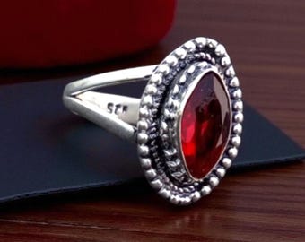 Può includere: Anello in argento con una grande gemma rosso scuro di forma ovale. La gemma è circondata da un bordo di perline. Il gambo dell'anello è diviso e presenta un piccolo marchio all'interno.