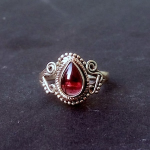 May include: A silver ring with a teardrop-shaped garnet gemstone set in a decorative filigree design.
