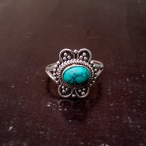 May include: A silver ring with a turquoise stone set in a floral design.