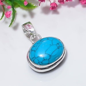 May include: An oval-shaped pendant featuring a bright turquoise stone with dark veining, set in a polished silver-toned metal frame. The pendant includes a sturdy silver-toned bail at the top for attachment to a chain or cord, showcasing a smooth finish.