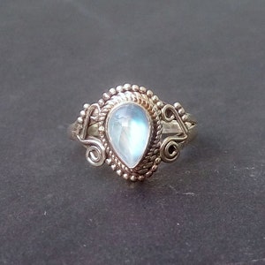 May include: A silver ring featuring a pear-shaped moonstone set in an intricate, ornate design.