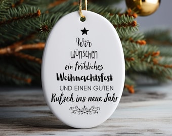 May include: White oval Christmas ornament with black text that reads "Wir wünschen ein fröhliches Weihnachtsfest und einen guten Rutsch ins neue Jahr".