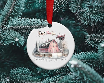 May include: A white ceramic Christmas ornament with a red barn, a red tractor, and a Santa Claus figure pulling a sleigh with cows. The text "Christmas On The Farm" is printed on the ornament.