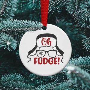 May include: White ceramic Christmas bauble featuring a black and white illustration of a person wearing a fur hat and glasses. The text "Oh Fudge!" is written in red.