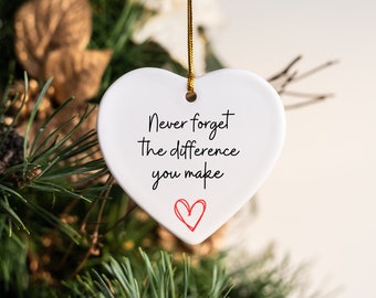 May include: White ceramic heart ornament with the text "Never forget the difference you make" and a small red heart in the center.