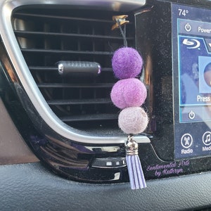 May include: Purple, lavender, and white felt ball car air freshener with a purple tassel hanging from a car vent.