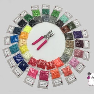 Könnte beinhalten: Eine Vielzahl von Farben kleiner runder Plastikknöpfe in einzelnen Beuteln, die in einem Kreis um eine Zange angeordnet sind. Die Beutel sind mit "best-size" beschriftet.