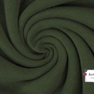 May include: Close-up of a dark green fabric with a ribbed texture. The fabric is folded and twisted, creating a swirling pattern.