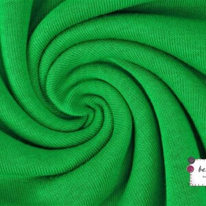 May include: Close-up of a bright green fabric with a textured surface. The fabric is folded and twisted, creating a swirling pattern.