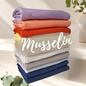 Könnte beinhalten: Ein Stapel gefalteter Musselinstoffe in verschiedenen Farben, darunter Lavendel, Pfirsich, Orange, Gelb, Beige, Weiß, Hellgrau und Marineblau. Das Wort Musselin ist in weißer Schreibschrift über die Mitte des Stoffstapels geschrieben.