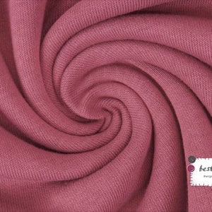 May include: Close-up of a soft, pink knitted fabric with a textured surface. The fabric is folded and twisted, creating a swirling pattern. A small white label with the text "best-size" is visible in the lower right corner.