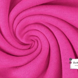 May include: Close-up of a bright pink fabric with a soft, textured surface. The fabric is folded and twisted, creating a swirling pattern.