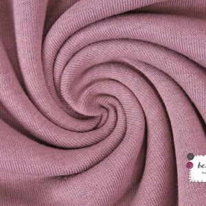 May include: Close-up of a soft, pink fabric with a textured surface. The fabric is folded and twisted, creating a swirling pattern.
