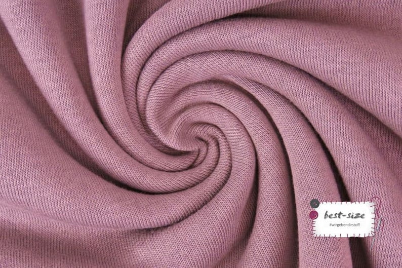 May include: Close-up of a soft, pink fabric with a textured surface. The fabric is folded and twisted, creating a swirling pattern.