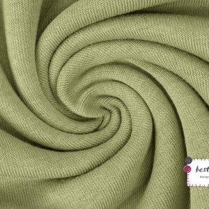 May include: Close-up of a soft, green fabric with a textured surface. The fabric is folded and twisted, creating a swirling pattern.