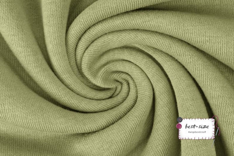 May include: Close-up of a soft, green fabric with a textured surface. The fabric is folded and twisted, creating a swirling pattern.