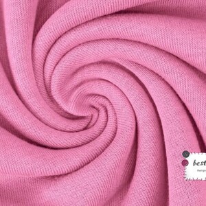 May include: Close-up of a soft, pink fabric with a textured surface. The fabric is folded and twisted, creating a swirling pattern.