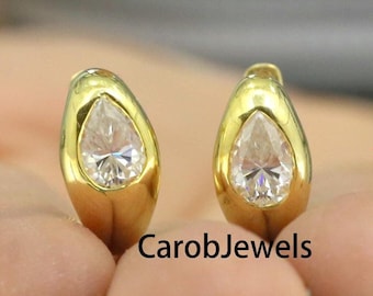 May include: A pair of gold teardrop earrings with clear pear-shaped gemstones. The earrings are shown in a close-up view.