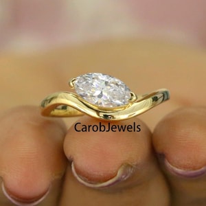 May include: A gold ring featuring a large oval-shaped diamond. The ring has a distinctive, curved design.