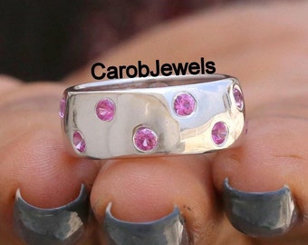 May include: A silver band ring with a hammered finish and pink gemstones set around the band. The text "CarobJewels" is visible on the ring.
