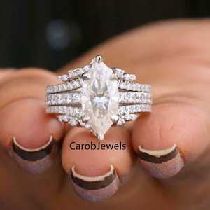 Puede incluir: Un anillo de plata con un gran diamante de forma marquesa, rodeado de diamantes más pequeños. El anillo está montado en una banda con varias filas de diamantes más pequeños.