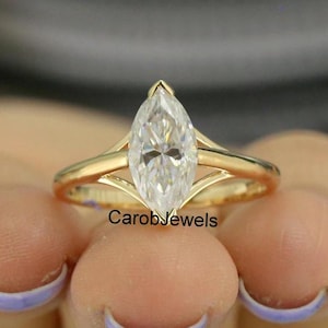 Könnte beinhalten: Ein goldener Verlobungsring mit einem Diamanten im Marquiseschliff. Der Ring hat ein geteiltes Schaftdesign und einen großen, klaren Edelstein. Der Text "CarobJewels" ist sichtbar.