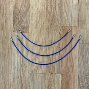 May include: Three blue circular knitting needles with silver tips. The needles are laid out in a curved shape on a wooden surface.