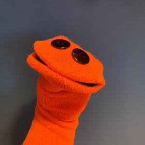 May include: Orange sock puppet with a wide open mouth and two black buttons for eyes.
