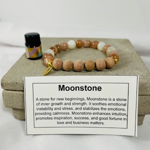 May include: A moonstone bracelet with wooden beads and a small bottle of essential oil. The card reads "Moonstone: A stone for new beginnings, Moonstone is a stone of inner growth and strength. It soothes emotional instability and stress, and stabilises the emotions, providing calmness. Moonstone enhances intuition, promotes inspiration, success, and good fortune in love and business matters."