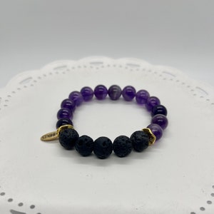 May include: A purple amethyst and black lava rock beaded bracelet with a gold charm that says "BRAVES".