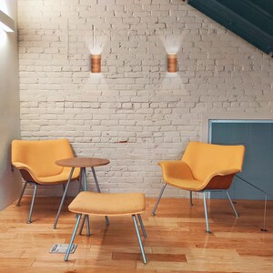 May include: Two yellow chairs with wooden frames and silver legs, a small wooden table, and a yellow ottoman in a room with a white brick wall and wood floors. Two wooden wall sconces are mounted on the wall.