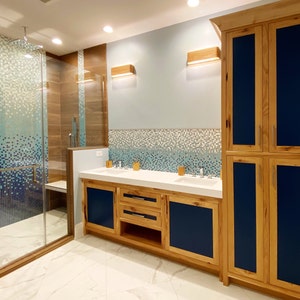 May include: A bathroom with a walk-in shower, double vanity with a white countertop, and a wooden cabinet with blue doors.