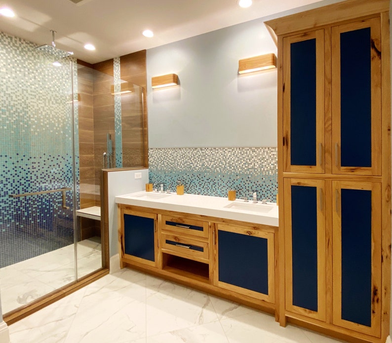 May include: A bathroom with a walk-in shower, double vanity with a white countertop, and a wooden cabinet with blue doors.