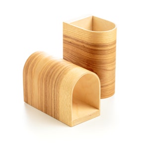 May include: Two wooden organizers with a natural wood grain finish. One organizer is a cylinder shape and the other is a curved shape with a hollowed-out section.