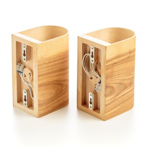 May include: Two wooden wall sconces with exposed wiring and a light switch on the back. The sconces are made of light brown wood with a natural grain pattern.