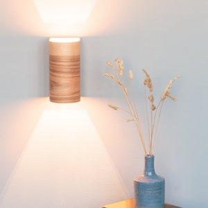 May include: A wooden wall sconce with a warm white light illuminates a small table with a blue vase filled with dried grasses and a stack of books.