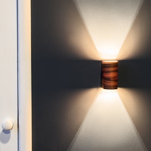 May include: A wooden cylindrical wall sconce with a warm white light shining down on a wooden surface.