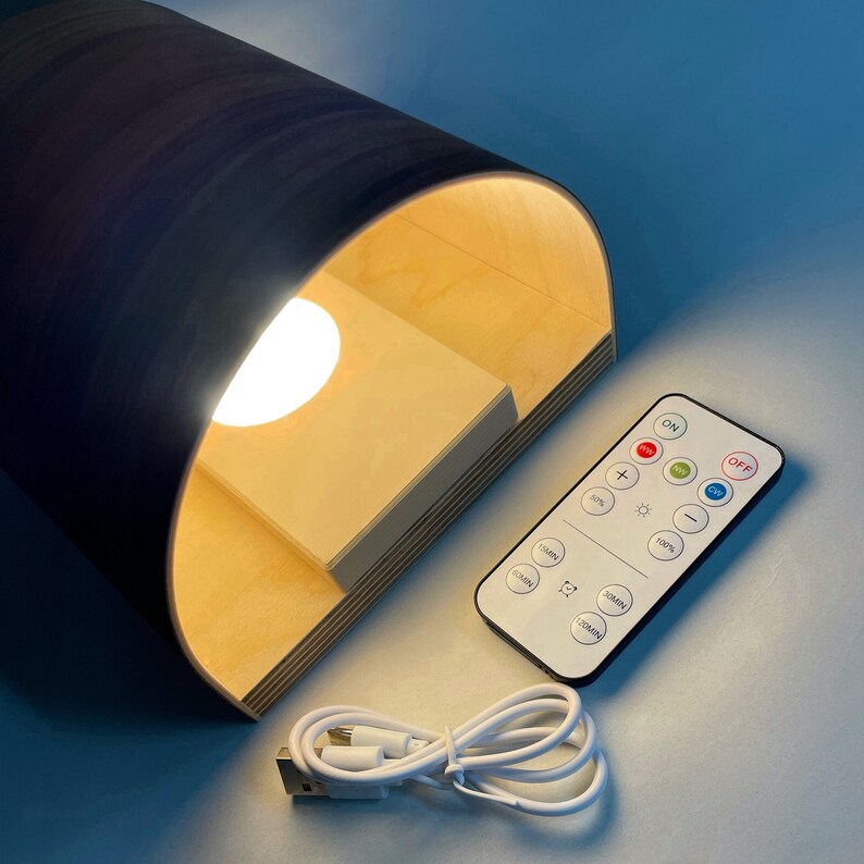 Puede incluir: Una l&aacute;mpara de madera con un dise&ntilde;o curvo y una bombilla blanca. La l&aacute;mpara se controla mediante un mando a distancia con botones para encender/apagar, brillo, temporizador y temperatura de color. La l&aacute;mpara est&aacute; conectada con un cable USB blanco.