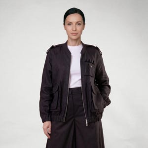 以下が含まれることがあります： 黒いボンバージャケット、白いTシャツ、黒いワイドパンツを着た女性。 ジャケットには複数のポケット、肩のエポレット、ジッパーが付いています。 全体的にモノクロで、ミニマリストな美学です。