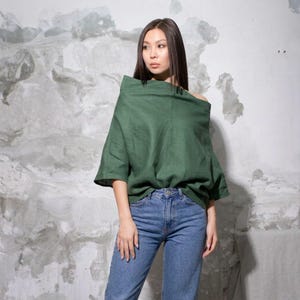 May include: A green off-the-shoulder top with short sleeves and blue jeans. The top is made of a soft, flowing fabric. The jeans are a classic blue wash.