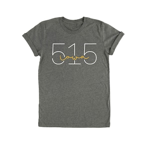 May include: Dark gray t-shirt with rolled-up sleeves. The shirt features the number "515" in white, with "Iowa" written in a yellow, cursive font underneath. A casual and comfortable style.