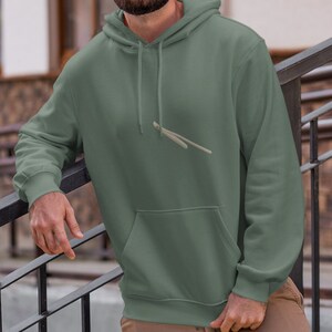 Könnte beinhalten: Eine Person trägt ein salbeigrünes Kapuzenpullover mit Kordelzug und lockerer Passform. Die Person steht auf einer Treppe mit einem schwarzen Metallgeländer.
