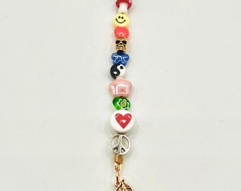 May include: A colorful beaded charm with a gold-tone clasp and cherry charm. The charm features various beads in shapes like hearts, smiley faces, and flowers. The beads are in a variety of colors, including blue, red, yellow, and green.