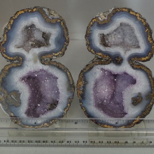 May include: Two halves of a geode with a purple amethyst crystal inside. The geode is cut in half and shows the crystal formation inside. The geode is about 6 inches in diameter.