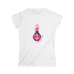 May include: A white short-sleeve t-shirt featuring a central graphic of a black potion bottle filled with glowing pink liquid, a pink heart stopper, and a small pink ghost rising above, with the text A little pink magic printed below.