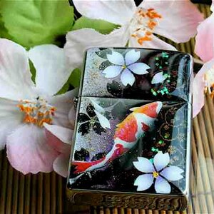 Peut inclure: Un briquet argenté avec un motif noir et blanc représentant un poisson-koi et des fleurs de cerisier. Le briquet a une finition brillante et irisée.