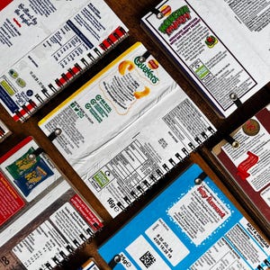 Puede incluir: Una colecci&oacute;n de ocho peque&ntilde;os cuadernos de espiral con diferentes cubiertas de envases de marcas de alimentos. Las cubiertas presentan marcas como Quavers, Monster Munch y Salt & Vinegar. Los cuadernos est&aacute;n todos cerrados y dispuestos en semic&iacute;rculo sobre una superficie de madera.