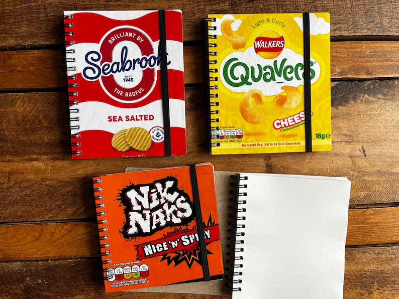 Puede incluir: Tres cuadernos de espiral con dise&ntilde;os de diferentes marcas de patatas fritas. El primer cuaderno es rojo y blanco con el logotipo de la marca Seabrook y el texto "Sea Salted". El segundo cuaderno es amarillo con el logotipo de la marca Walkers y el texto "Quaver's Cheese". El tercer cuaderno es naranja con el logotipo de la marca Nik Naks y el texto "Nice 'n' Spicy".