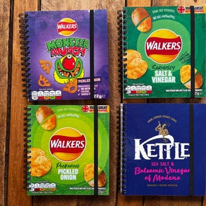 Puede incluir: Cuatro cuadernos de espiral diferentes con dise&ntilde;os de bolsas de patatas fritas. Los cuadernos presentan las marcas Walkers, Kettle y Monster Munch. Los cuadernos son todos azules, verdes y morados.